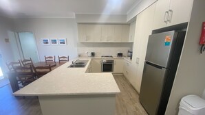 A modern kitchen with a central island, white cabinetry, a stainless steel refrigerator, and a dining area with wooden chairs.