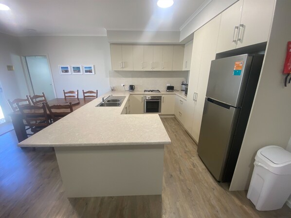 Una cucina moderna con isola centrale, mobili bianchi, frigorifero in acciaio inossidabile e zona pranzo con sedie in legno.