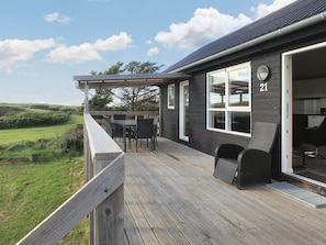 A wooden deck with outdoor furniture, a large window, and a view of the landscape.