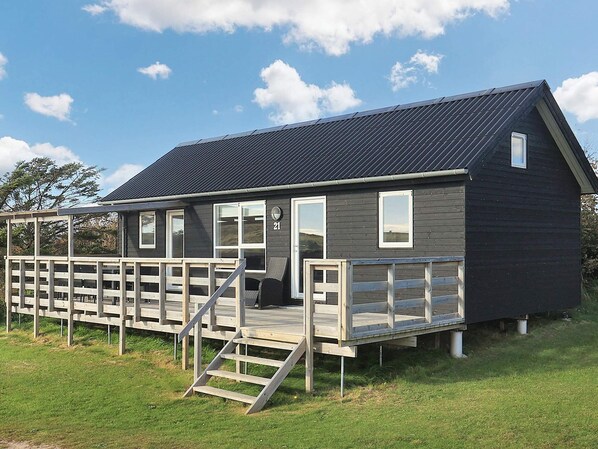 A small, dark-colored cabin with a wooden deck and a staircase leading to the entrance.