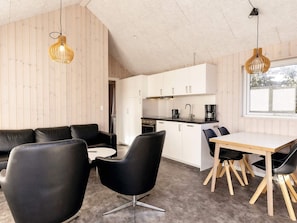 A modern kitchen with white cabinets, a black countertop, and a coffee maker. There is a dining area with a wooden table and black chairs.
