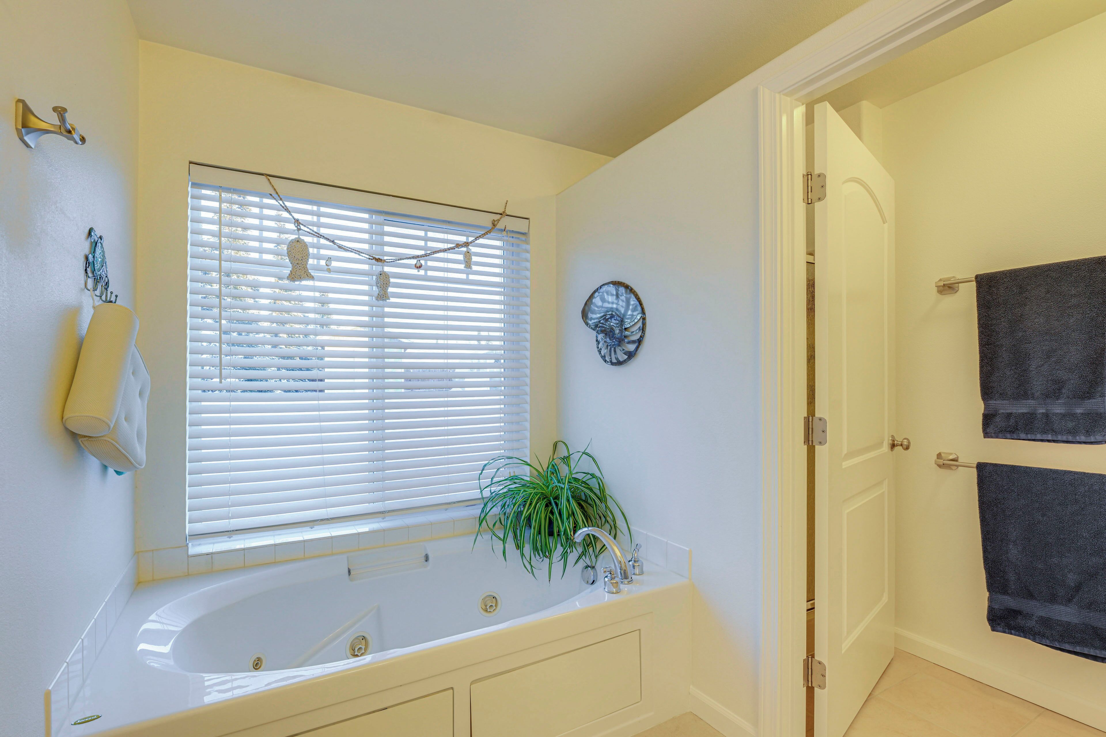Un baño con una bañera blanca, una ventana con persianas, una planta en maceta y un perchero.