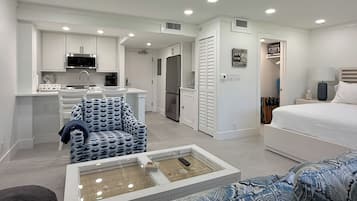 A compact living space with a kitchenette, a dining area, a bedroom, and a seating area with a glass-top coffee table.