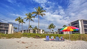 A beach with palm trees, a colorful umbrella, and beach chairs.