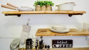Un comptoir de cuisine aménagé en coin café, avec une machine à café, des tasses et un panneau indiquant : « mais avant toute chose… CAFÉ ».