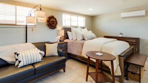 Une chambre à coucher moderne avec un lit, un canapé, une petite table et une lampe fixée au mur.