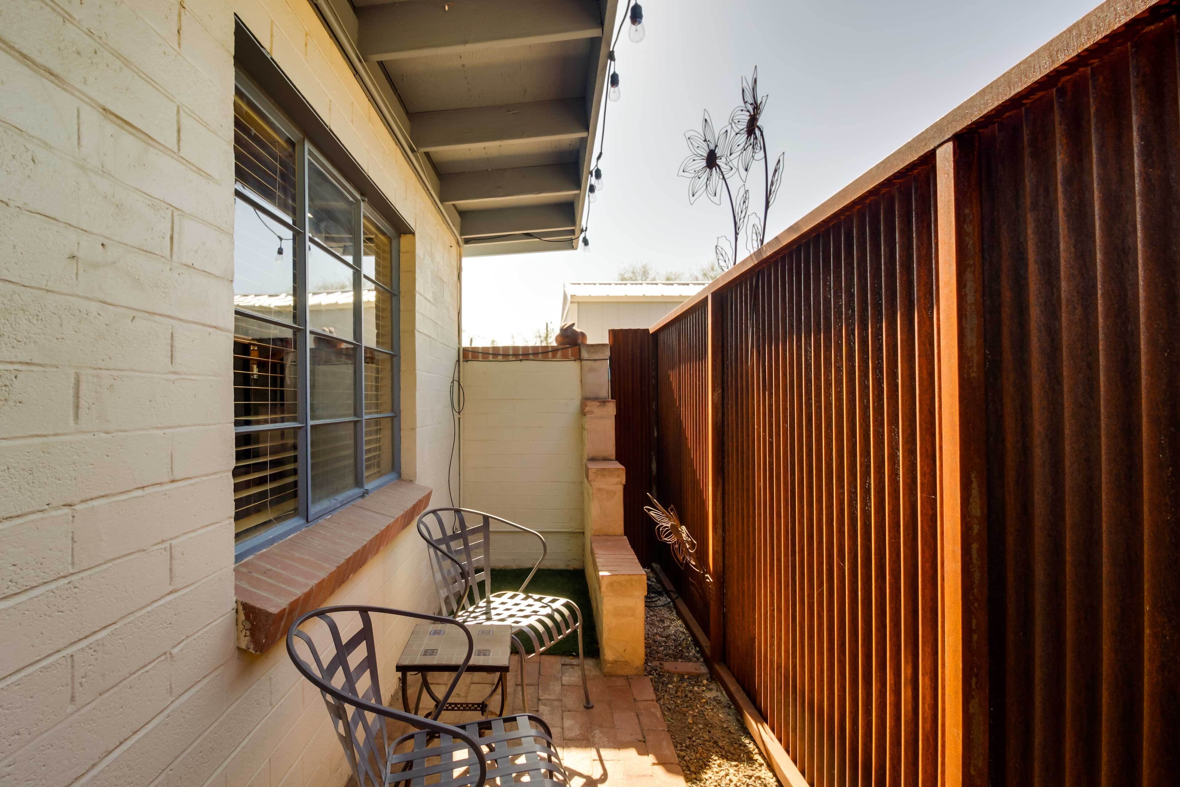 A patio with two metal chairs and a table, a wooden fence, and a window with blinds.