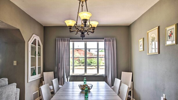 Une salle à manger avec une table en bois, des chaises, un lustre et une fenêtre avec des rideaux.