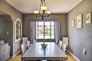 Una sala da pranzo con un tavolo in legno, sedie, un lampadario e una finestra con tende.