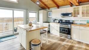 Une cuisine spacieuse avec des poutres en bois, un grand îlot central et une vue sur l’extérieur.