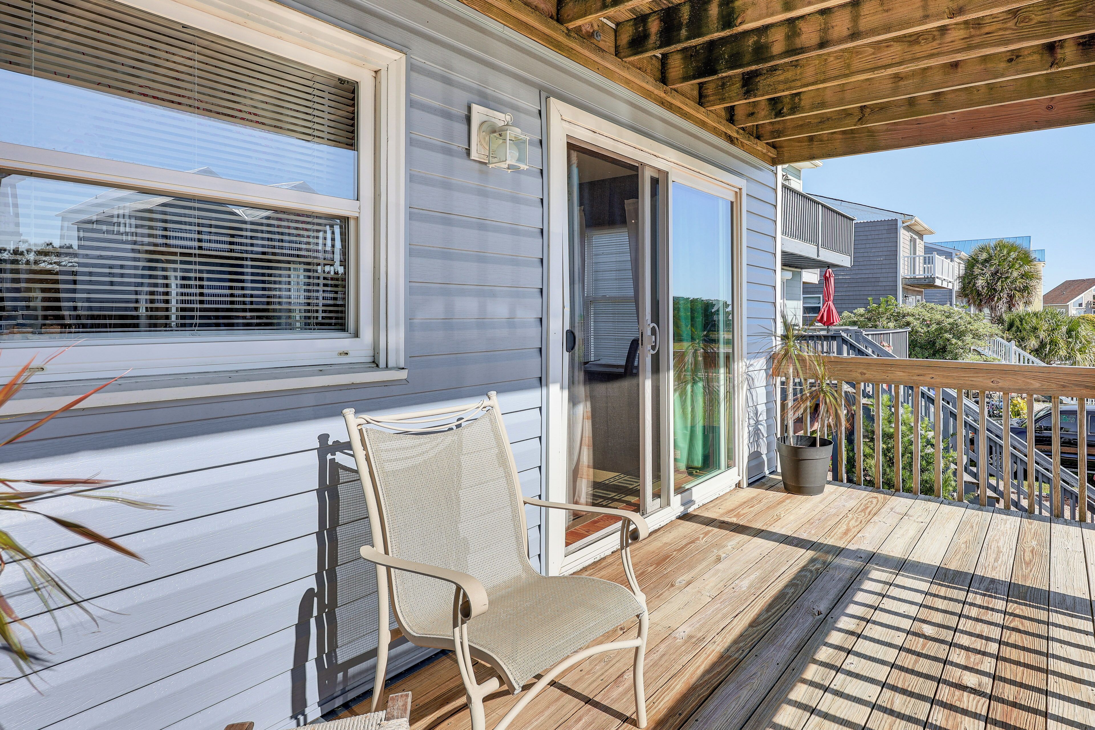 Een houten terras met een stoel, een schuifdeur en uitzicht op omliggende huizen.