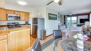 A modern kitchen with wooden cabinets, stainless steel appliances, and a dining area with a glass table and chairs. - Walk to Beach: Duplex in North Topsail Beach! (Sneads Ferry)
