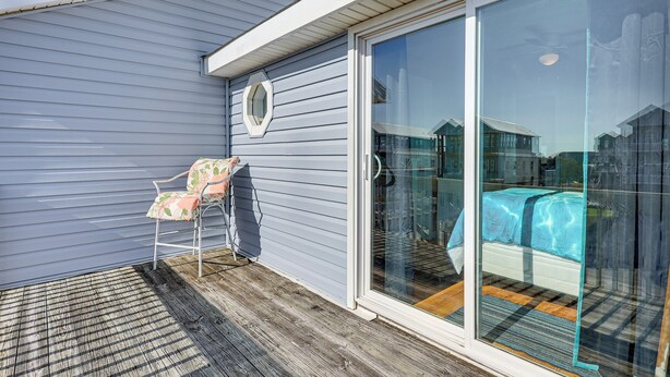 A room with a sliding glass door, a bed with a blue cover, and a chair with a floral cushion. - Walk to Beach: Duplex in North Topsail Beach! (Sneads Ferry)