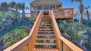 Eine Holztreppe führt zu einem Strandhaus mit einem Balkon.