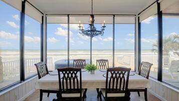 A conservatory with a table and chairs, a chandelier, and a view of the beach.