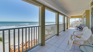 Ein überdachter Balkon mit weißen Stühlen und einem Tisch, mit Blick auf Strand und Meer.
