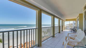 Un balcone coperto con sedie e tavolo bianchi, con vista su una spiaggia e l'oceano.