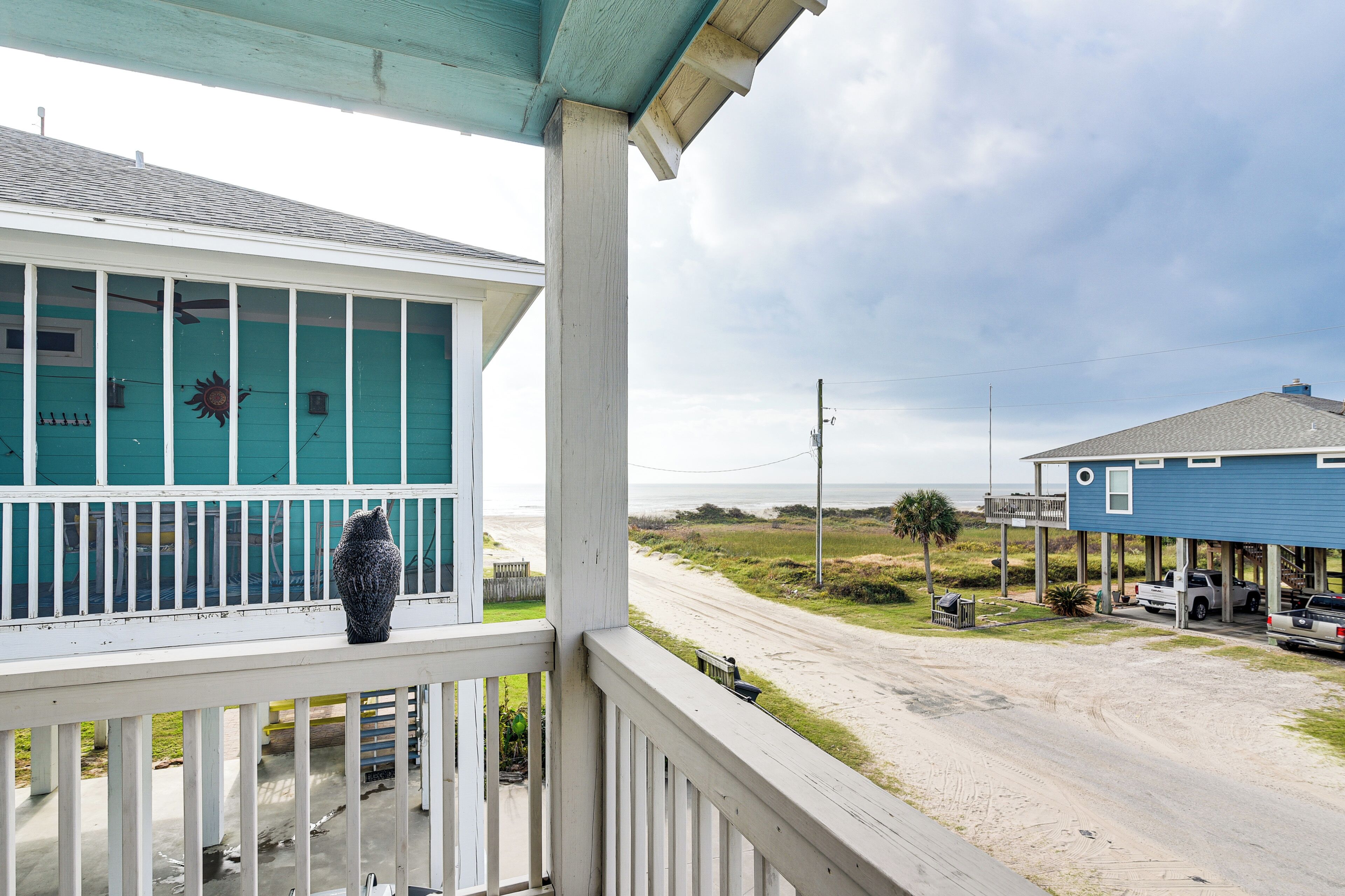 A porch with a decorative vase, a view of a beach, and a blue house with a white railing.