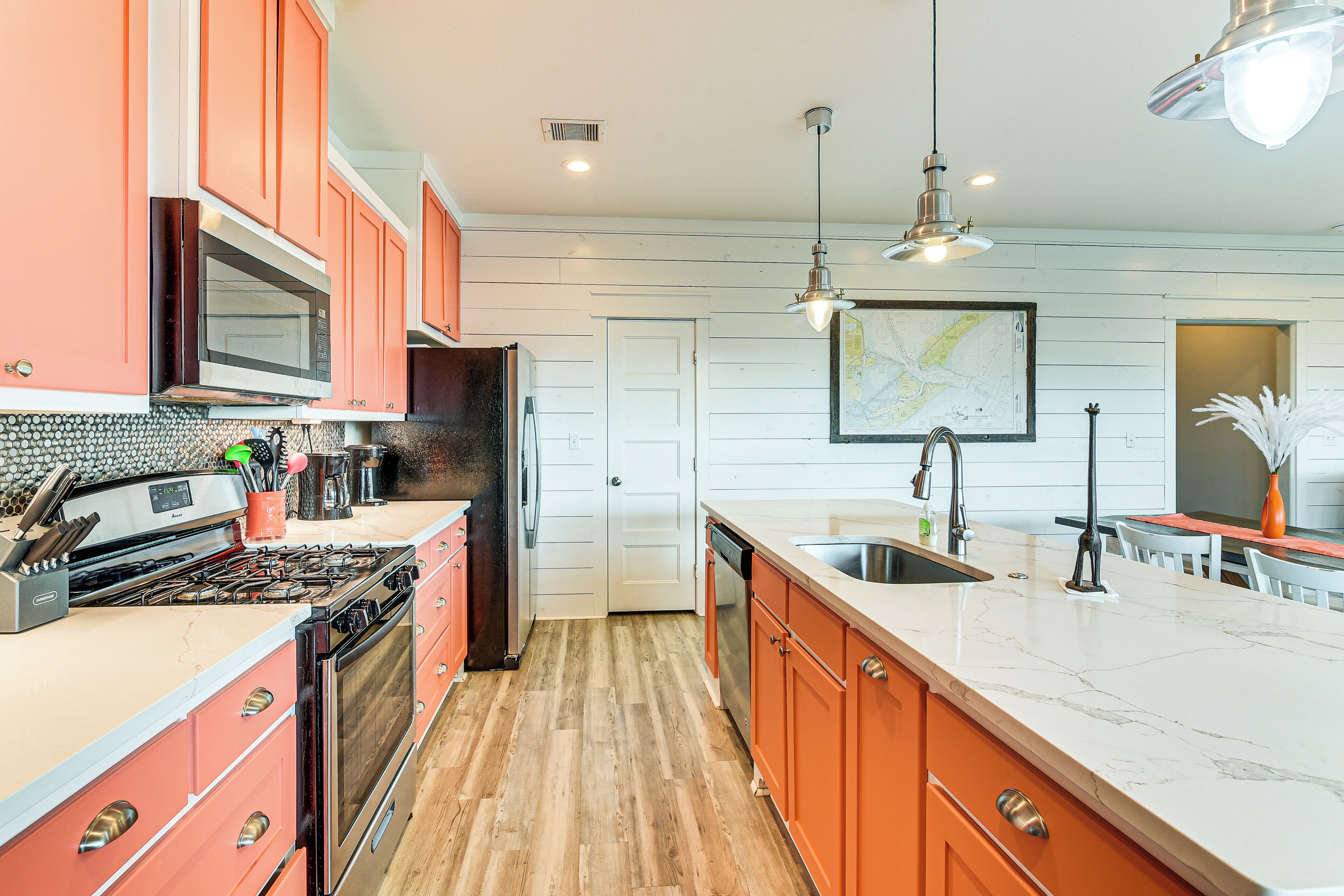 Une cuisine avec un plancher en bois, un grand îlot central doté d’un évier et des meubles de couleur orange.