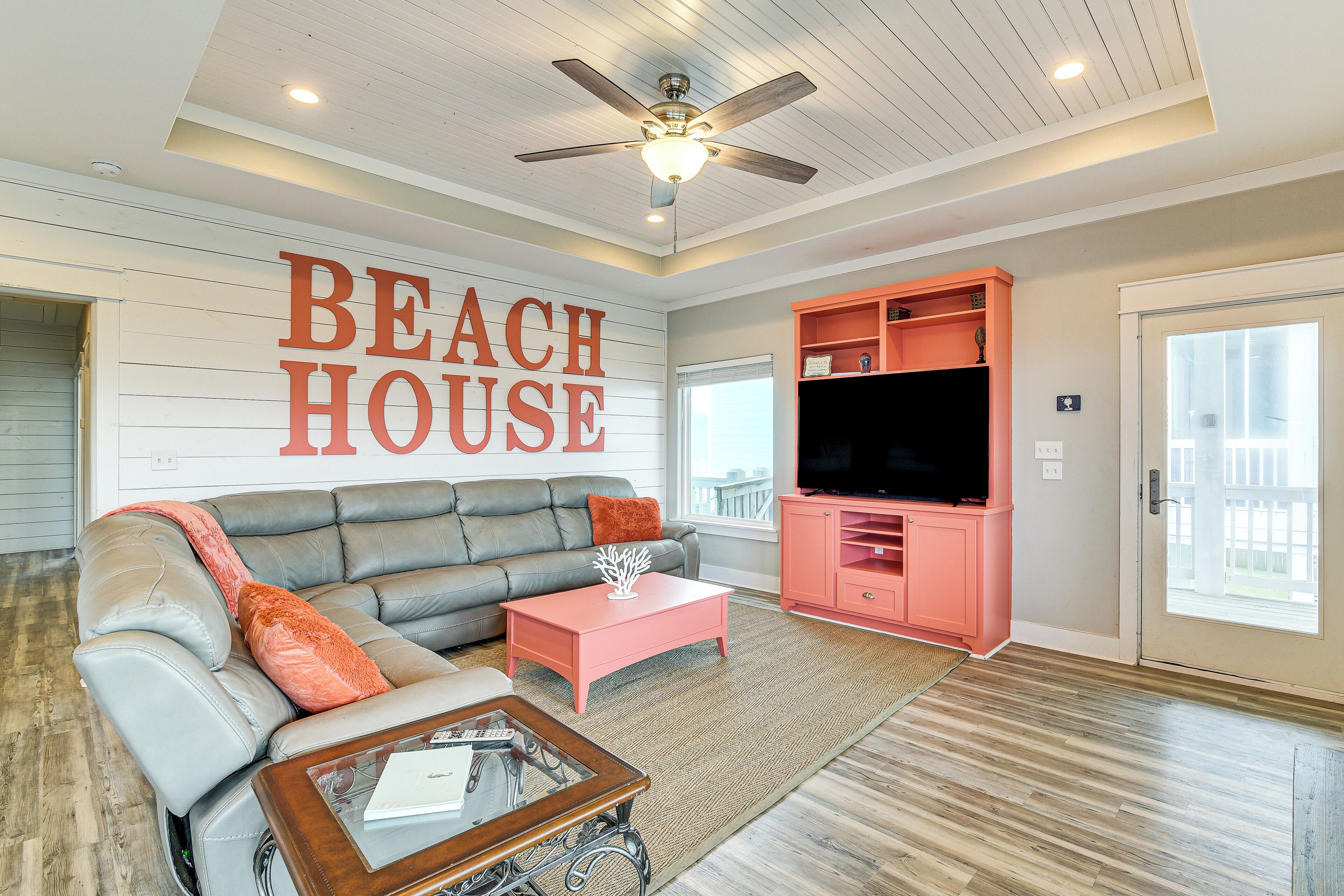 A living room with a gray sectional sofa, a pink coffee table, and a television in a pink cabinet.