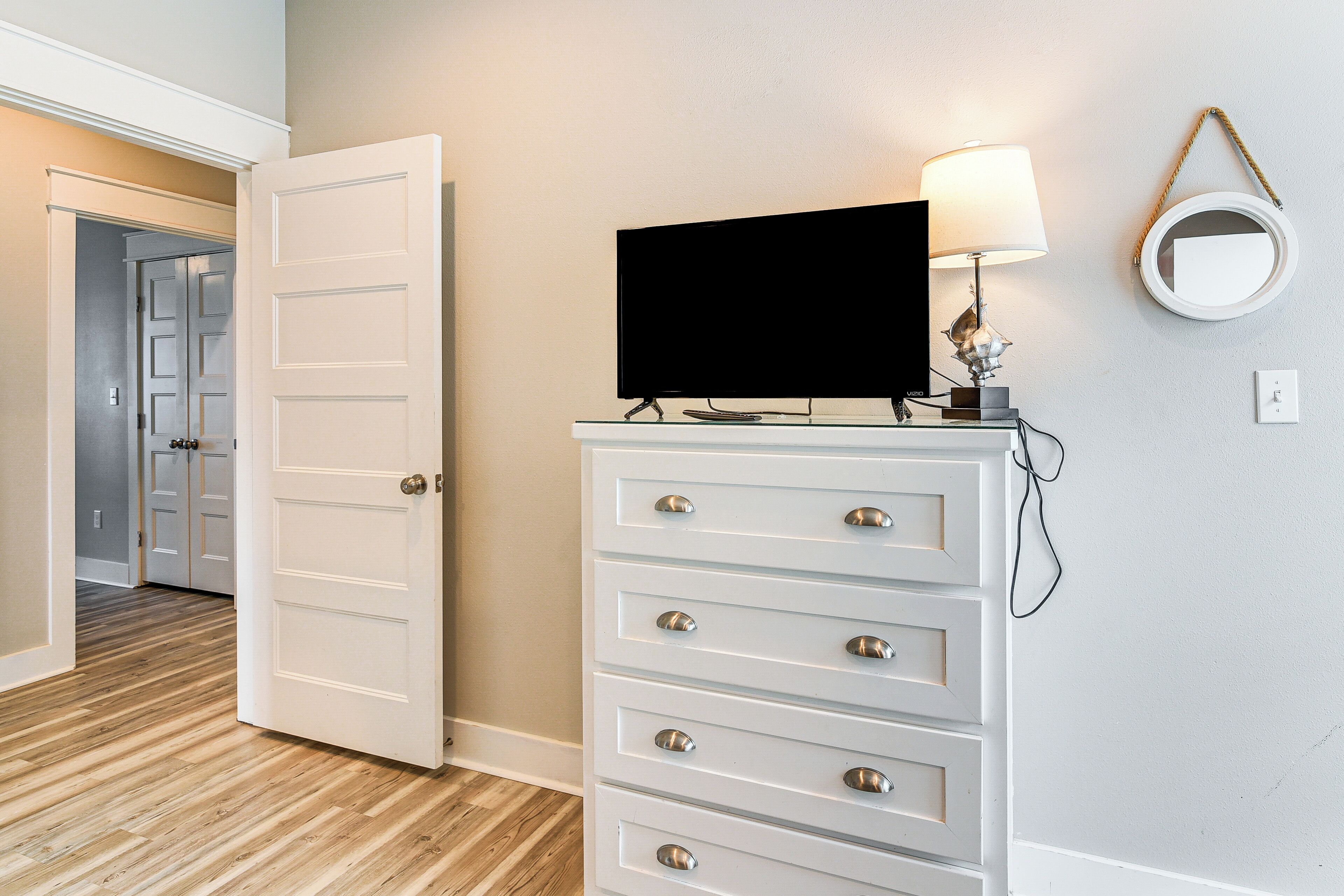 A room with a white dresser, a television on top, a lamp, and a mirror on the wall.