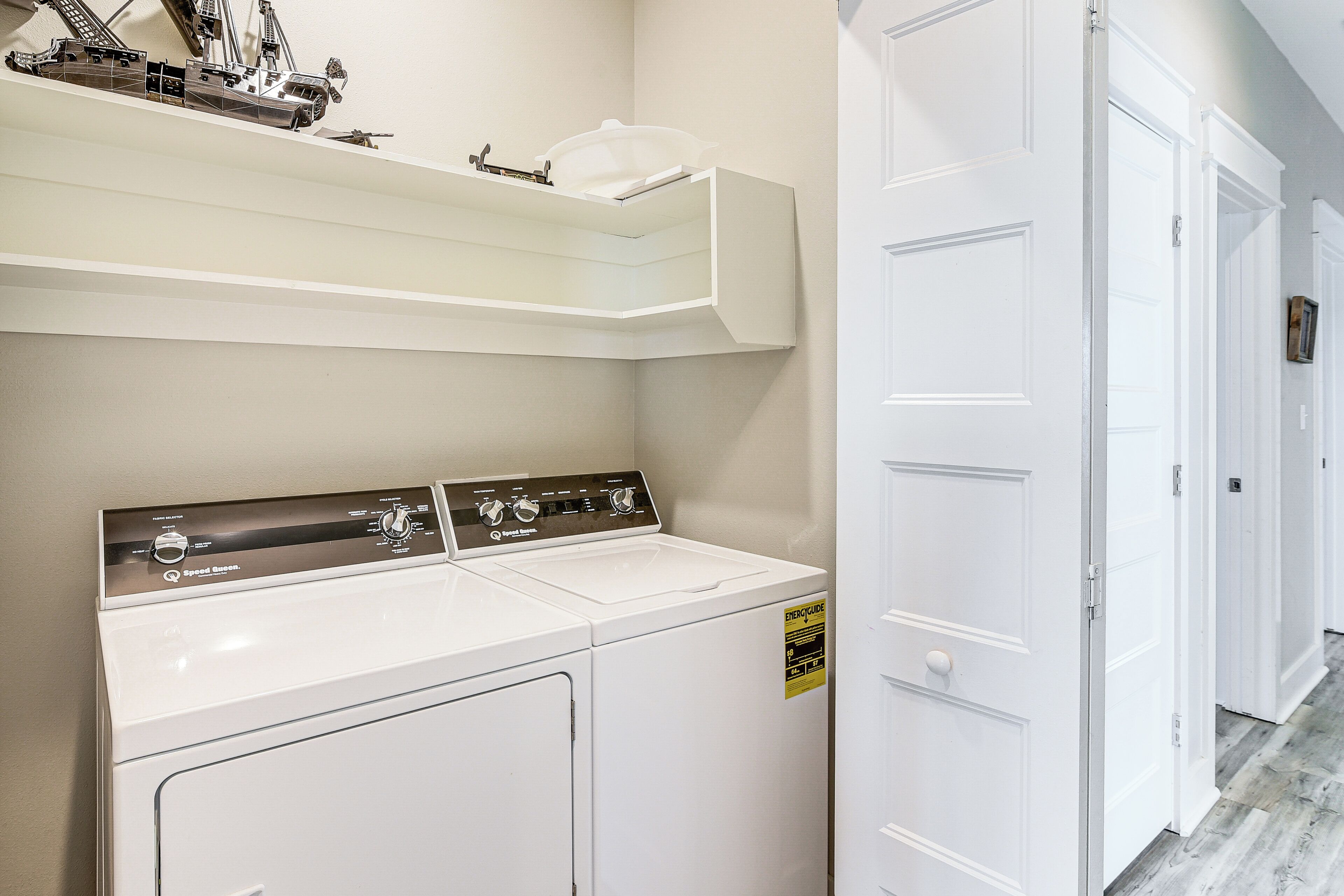 A laundry area with two white washing machines, a shelf above, and a white door to the right.