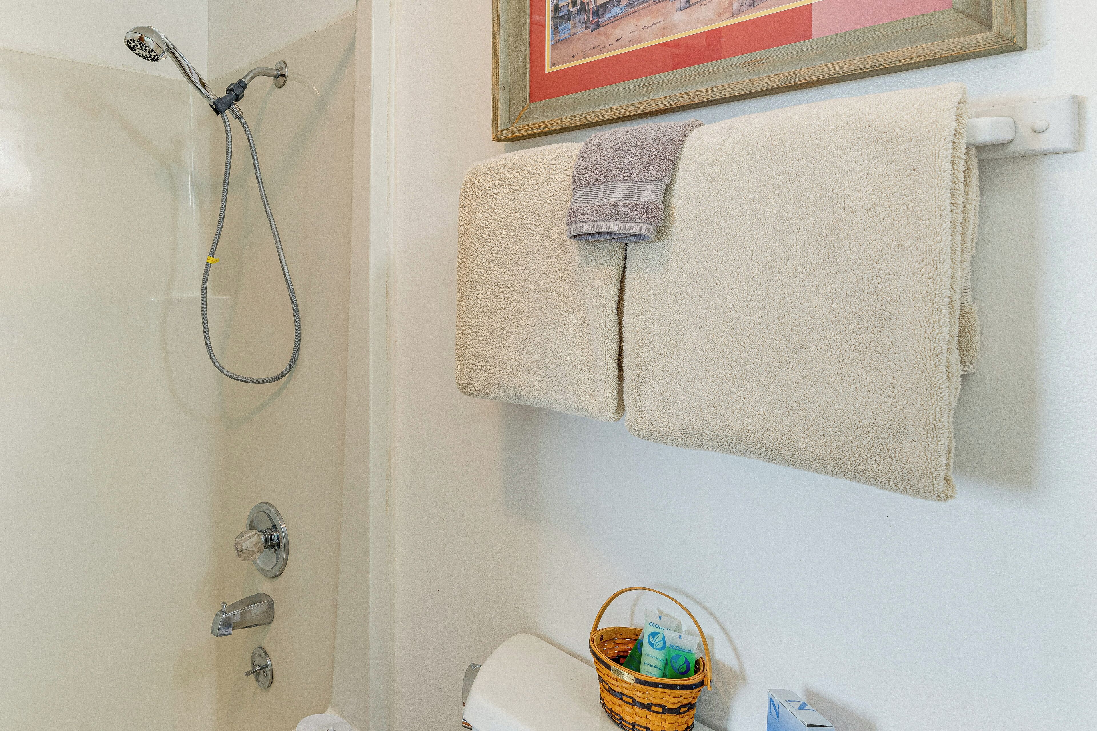 A bathroom with a shower, a toilet, a towel rack with two towels, and a basket with toiletries.