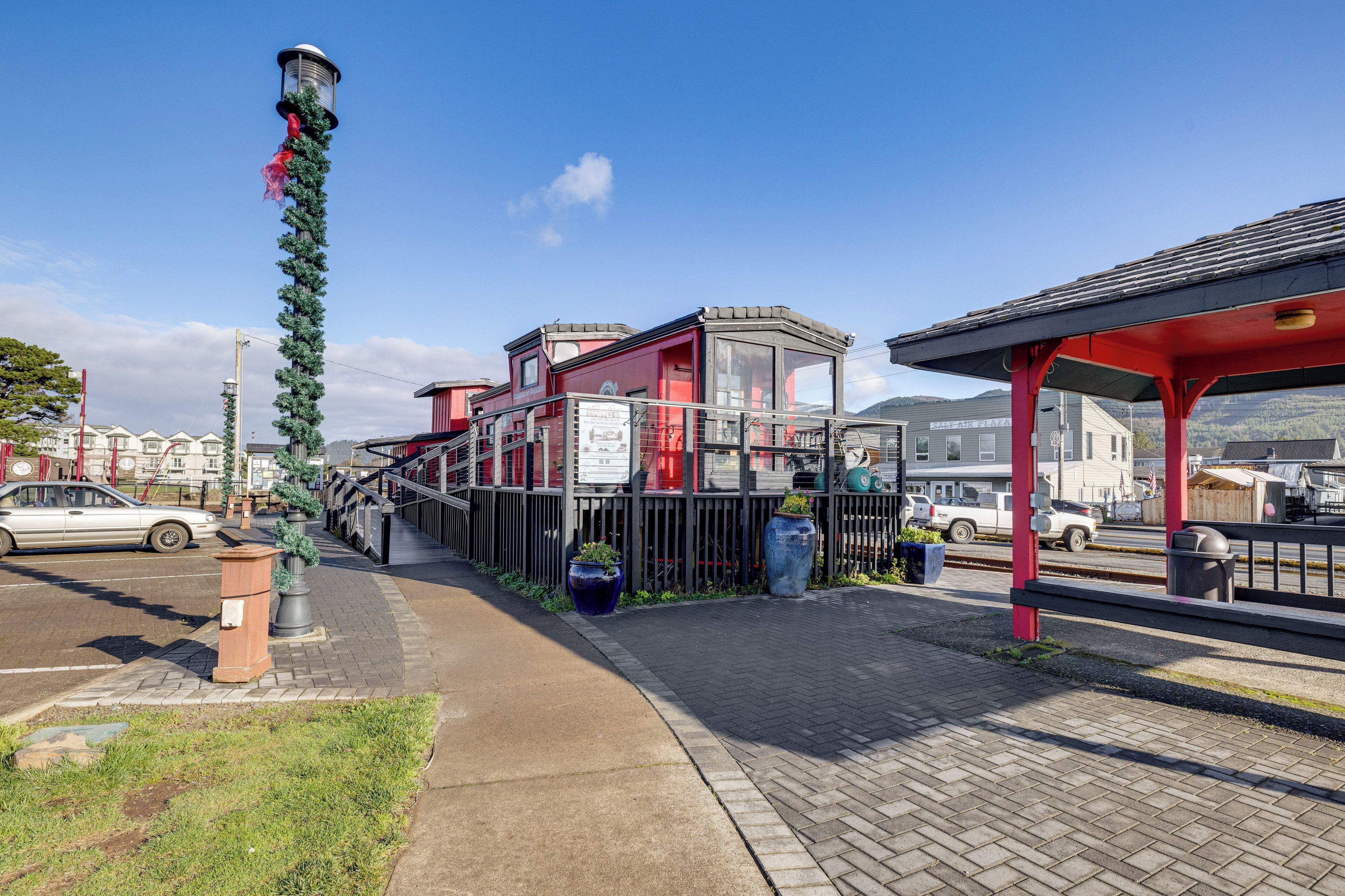 A train station platform with a red shelter, a clock tower, and a row of houses in the background.