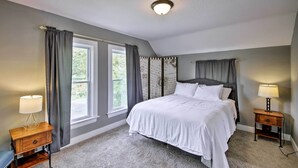 A bedroom with a large bed, two bedside tables, a nightstand, a window with curtains, and a ceiling light. - Lakeside Garden Home - 1 Mile to Main Street! (Fort Wayne)