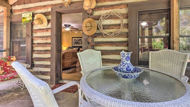 A rustic wooden cabin with a glass table and wicker chairs, surrounded by logs and a woven wreath. - Rustic-yet-cozy Cabin w/ Patio, 12 Mi to Asheville (Arden)