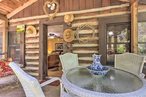 A rustic wooden cabin with a glass table and wicker chairs, surrounded by logs and a woven wreath. - Rustic-yet-cozy Cabin w/ Patio, 12 Mi to Asheville (Arden)
