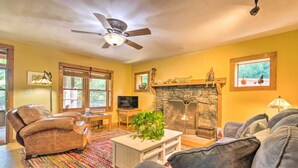 A cozy living room with a fireplace, a ceiling fan, and a television. - Rustic-yet-cozy Cabin w/ Patio, 12 Mi to Asheville (Arden)