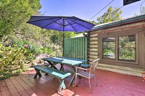 A wooden deck with a picnic table and chairs, a blue umbrella, and a rustic cabin with windows. - Rustic-yet-cozy Cabin w/ Patio, 12 Mi to Asheville (Arden)