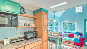 Una cocina con armarios de madera, un microondas, un tostador y una radio antigua. Hay un comedor con una alfombra colorida y un sofá rojo.