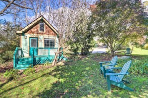 A small wooden cabin with a porch and two Adirondack chairs in a garden setting.