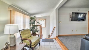 A living room with a sofa, a table with a lamp, a potted plant, a staircase, and a TV mounted on the wall. - Old Orchard Beach Apt - Walk to Beach & Pier! (Old Orchard Beach)