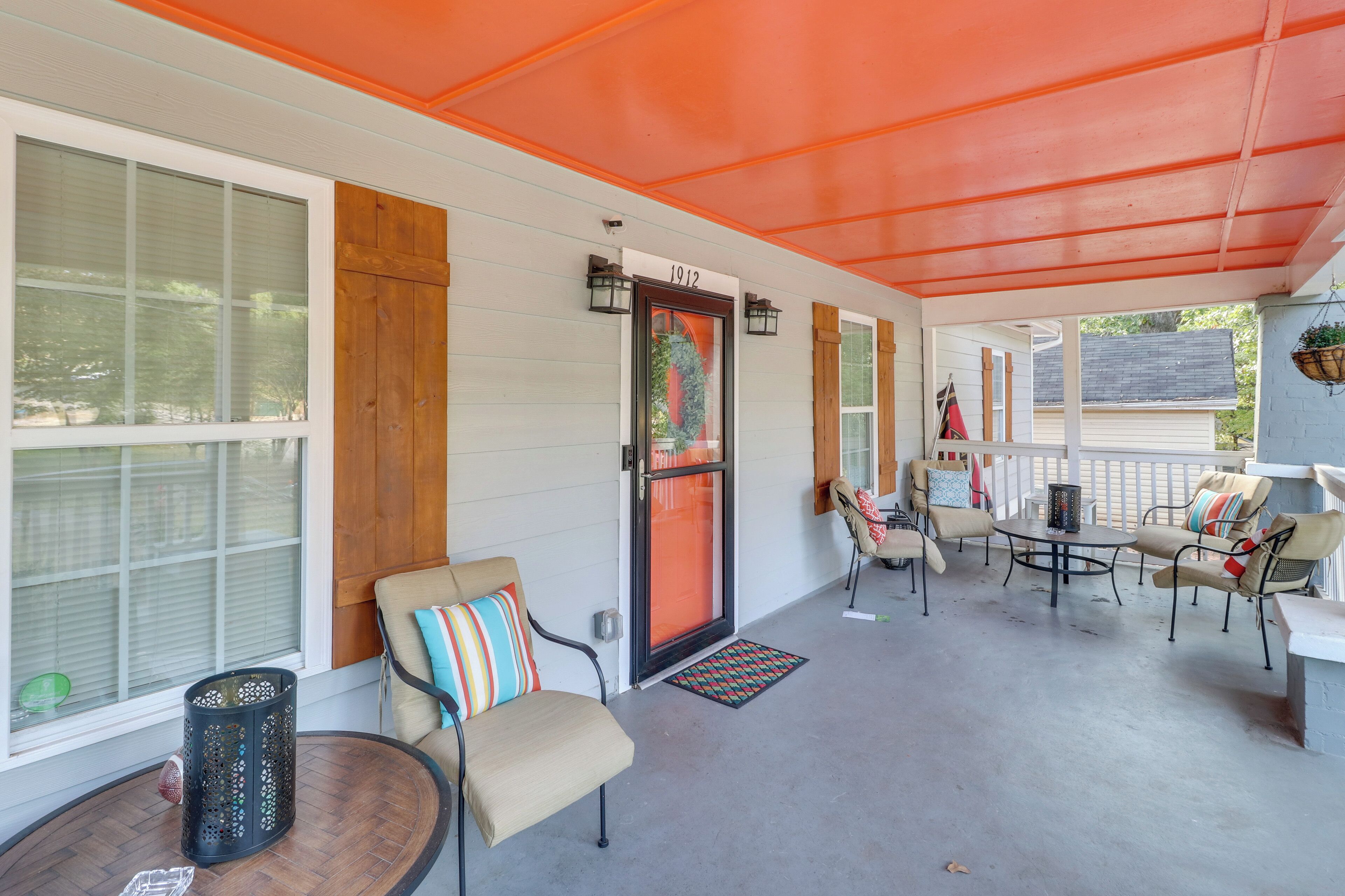 A covered porch with a wooden door marked "1912," outdoor seating with cushions, and a hanging planter.