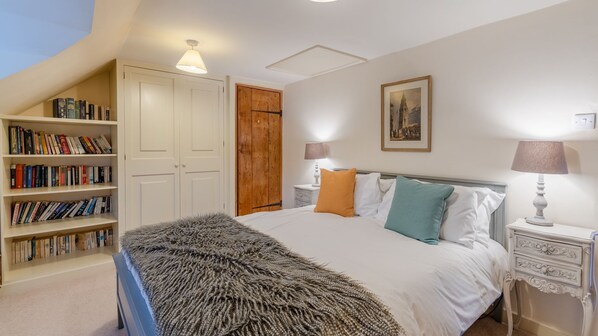 A bedroom with a large bed, a bookshelf, a wooden wardrobe, and a painting on the wall.