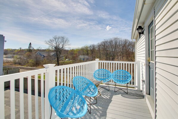 A wooden deck with a white railing, three blue chairs, and a view of houses and trees in the background. - Apt in Old Orchard Beach - Walk to Bay + Pier (Old Orchard Beach)
