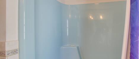 A corner of a room with a light blue wall, a shower area, and a door with a purple curtain.