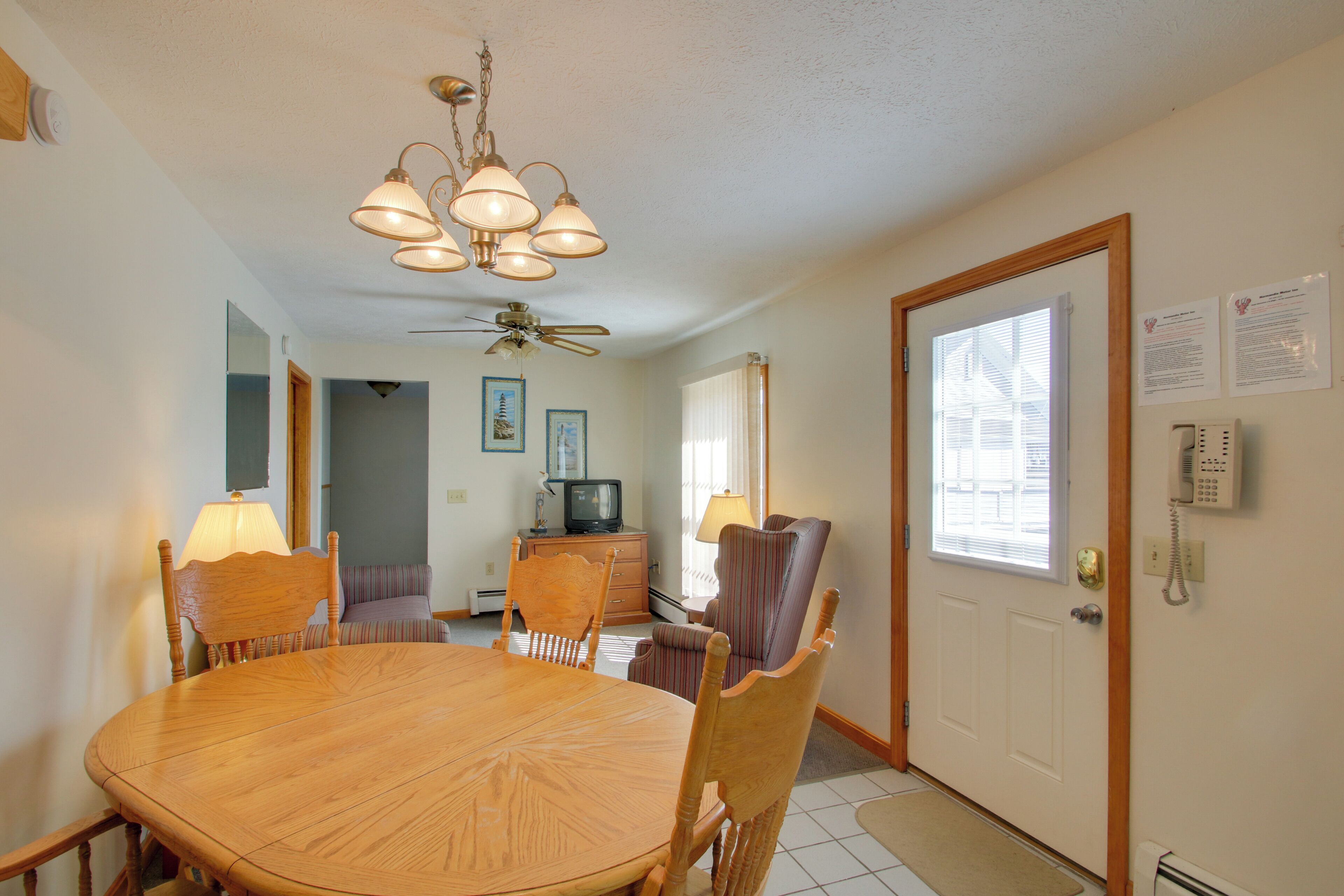 A dining area with a round wooden table, chairs, a ceiling fan, and a chandelier.