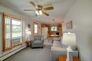 A living room with a ceiling fan, a houndstooth armchair, a white sofa, and a dining area with a chandelier. - Apt in Old Orchard Beach - Walk to Bay + Pier (Old Orchard Beach)