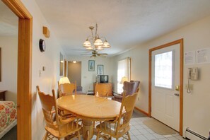 A dining area with a round wooden table, chairs, a ceiling fan, and a television in the background. - Apt in Old Orchard Beach - Walk to Bay + Pier (Old Orchard Beach)