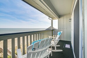 A covered outdoor area with two white lounge chairs and a small table, overlooking a beach.