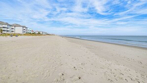A wide sandy beach with footprints, a clear blue sky, and buildings in the background. - Oceanfront Condo w/ Pool Access in Surfside Beach! (Surfside Beach)