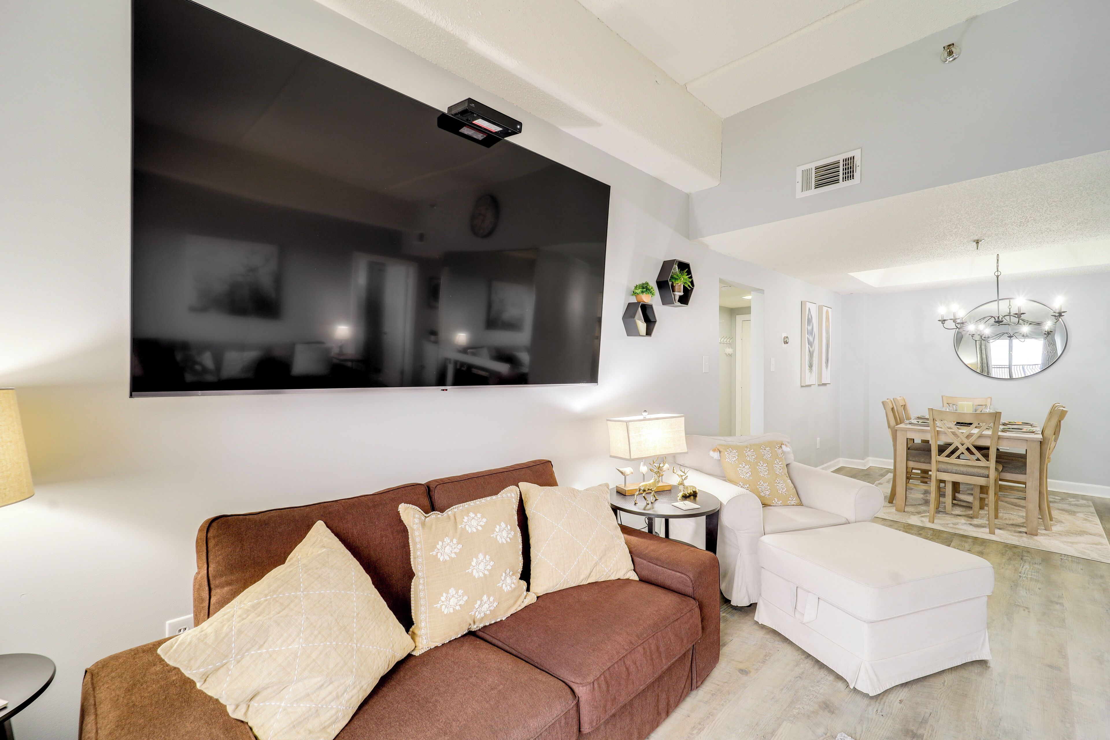 Un salon avec un canapé marron, un fauteuil blanc et un coin repas comprenant une table et des chaises en bois.