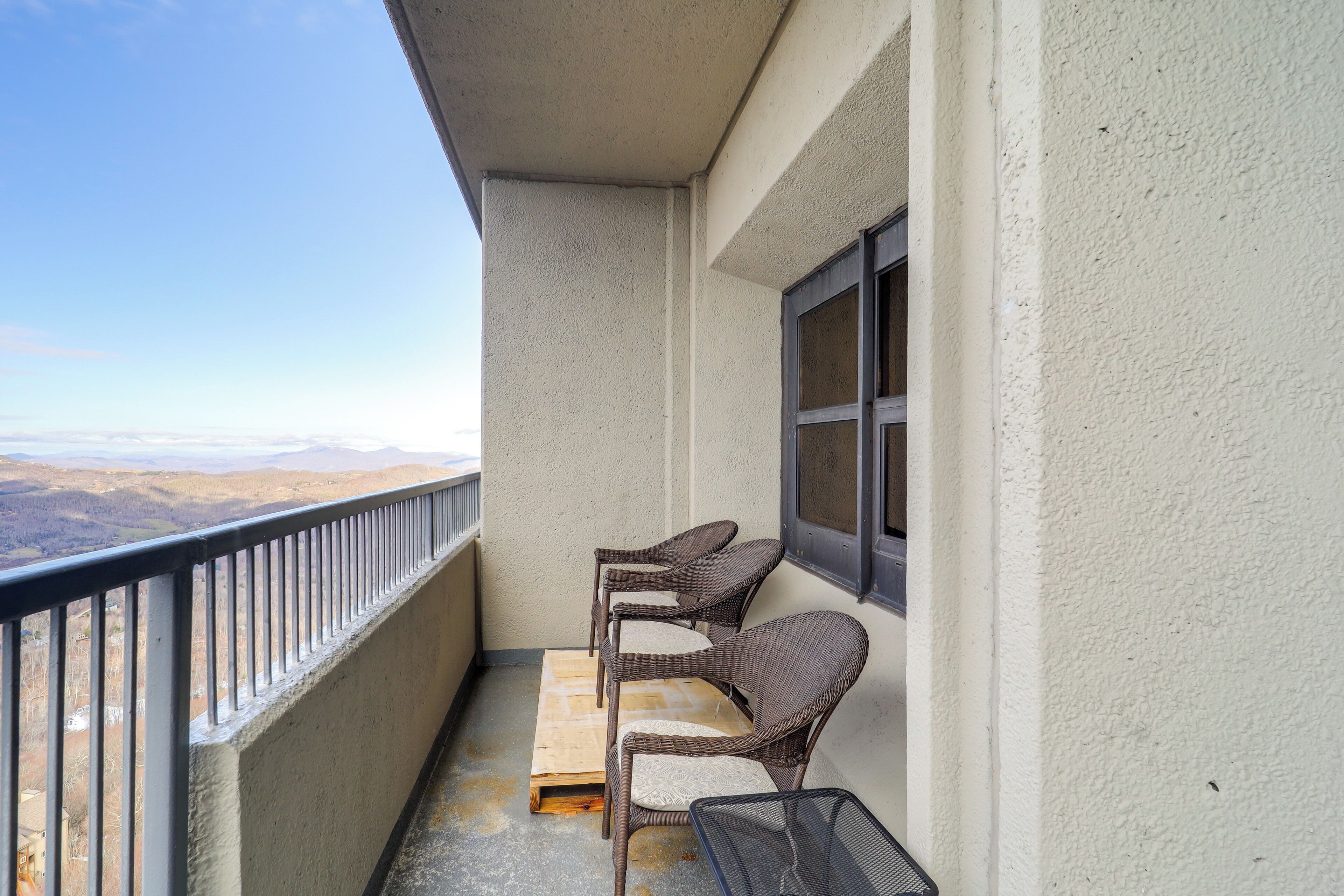 Un balcón con sillas de mimbre y un banco de madera, con vistas a un paisaje montañoso.