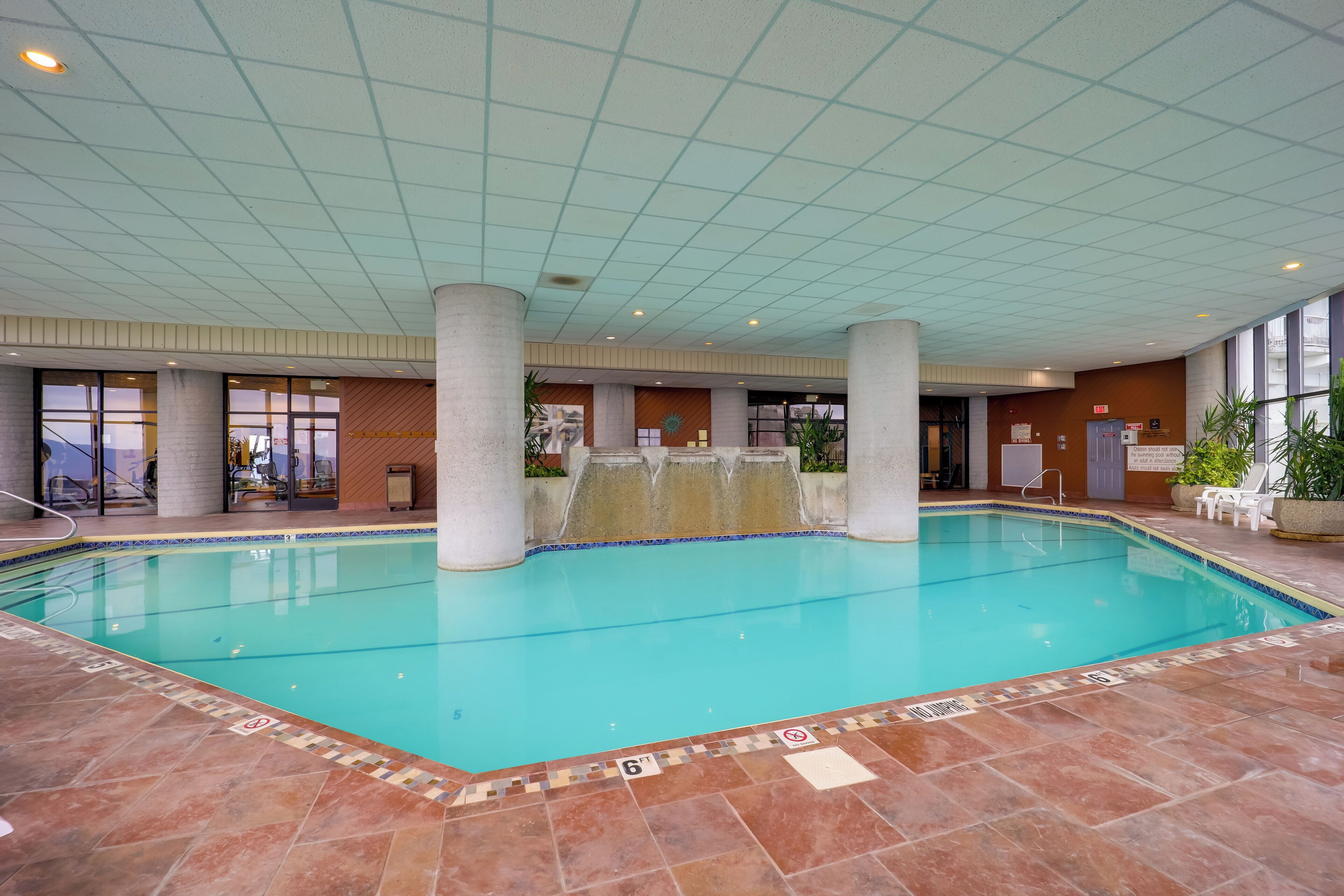 An indoor swimming pool with clear water, tiled floor, and a tiled ceiling.