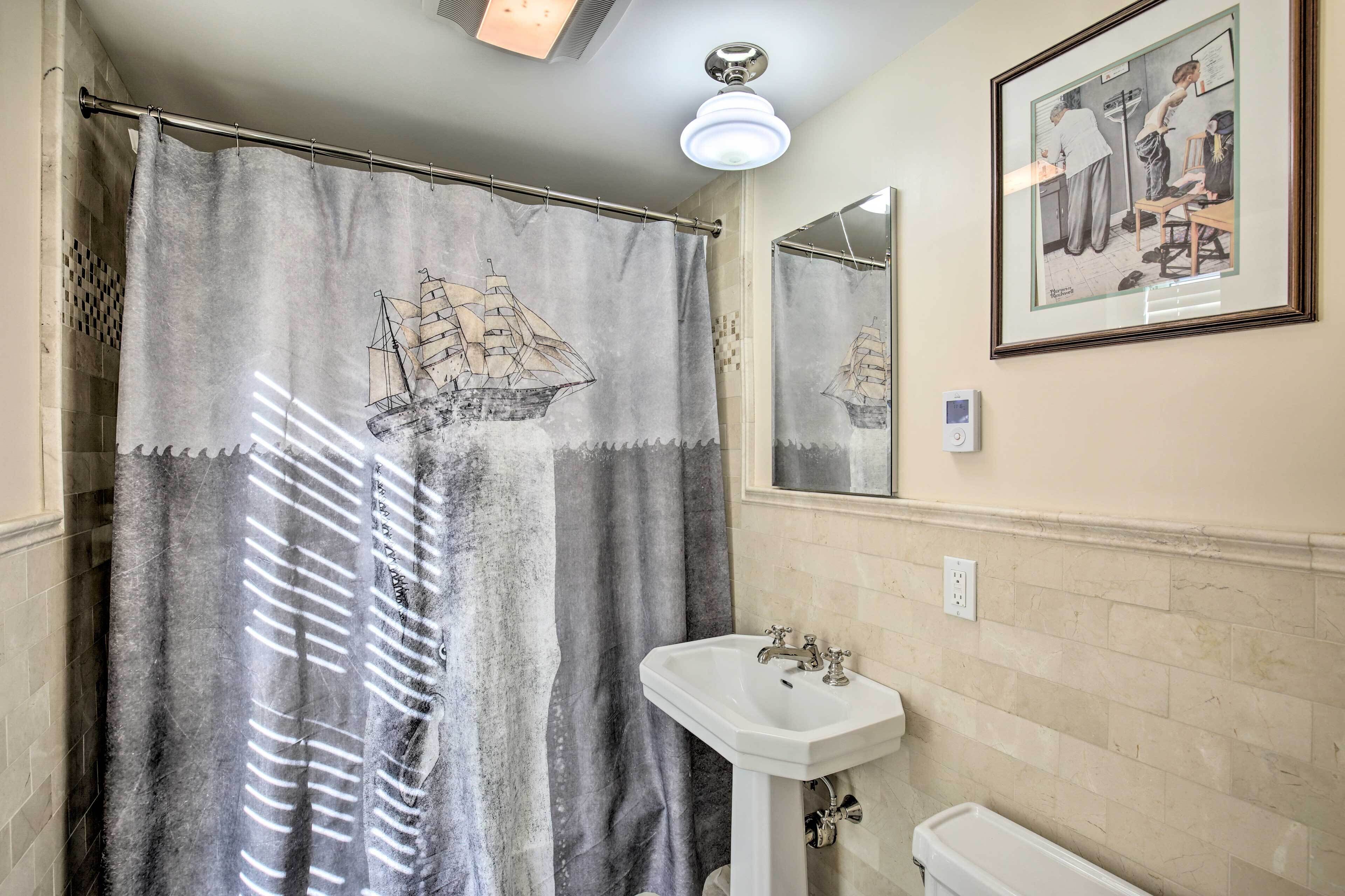 A bathroom with a ship-themed shower curtain, a sink, and a framed picture on the wall.