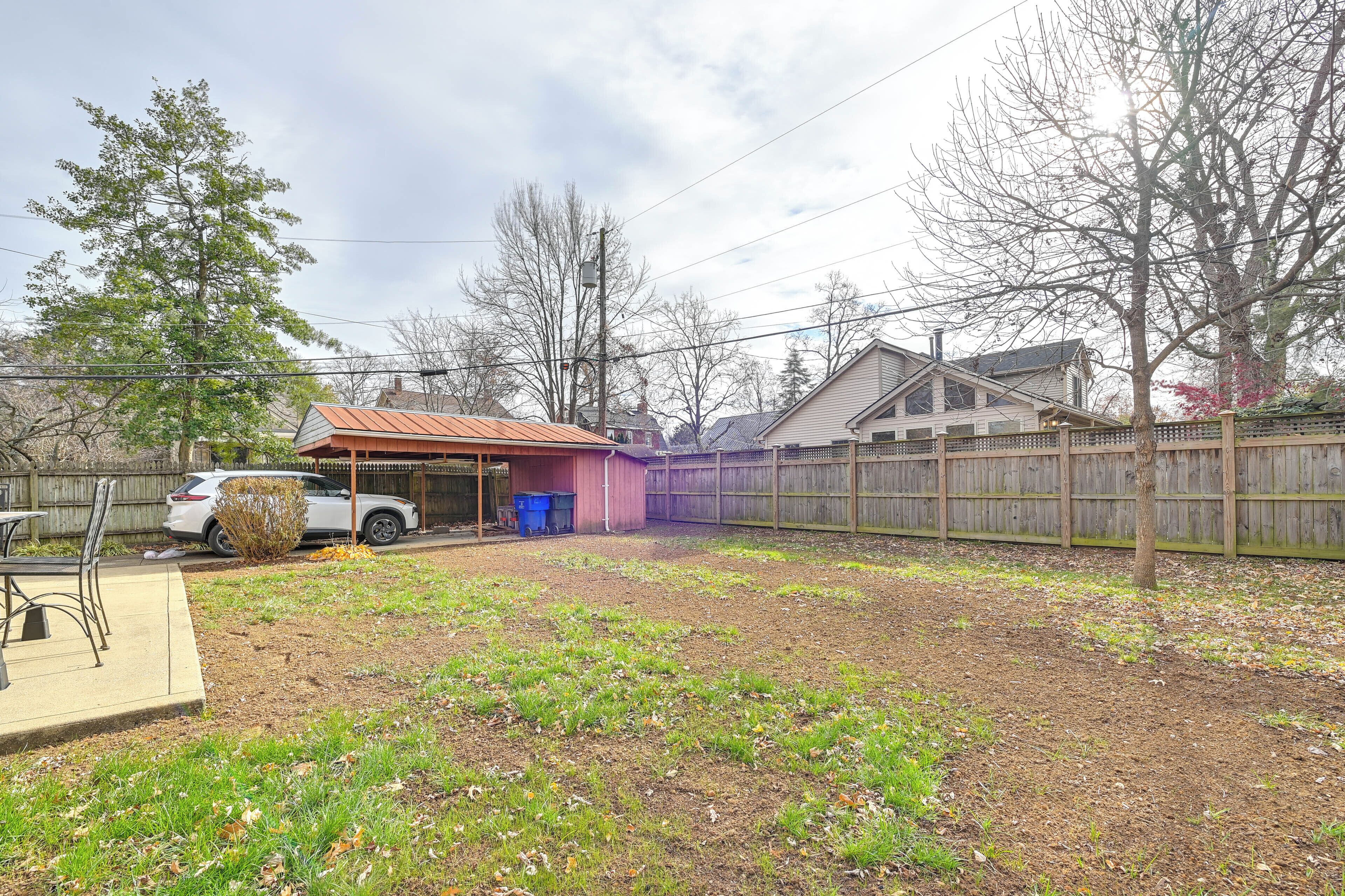 A backyard with a covered patio area, a wooden fence, and a car parked nearby.